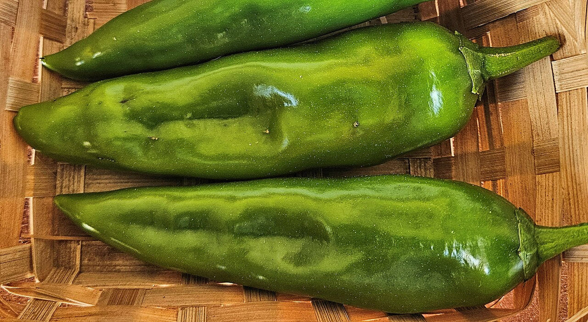 Three long green Anaheim peppers on a wooden surface