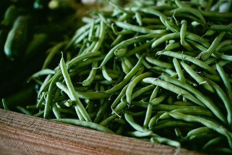 A pile of slender green snap beans in a wooden market box