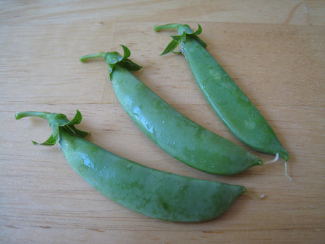 Three plump green snap-pea pods on a wooden board